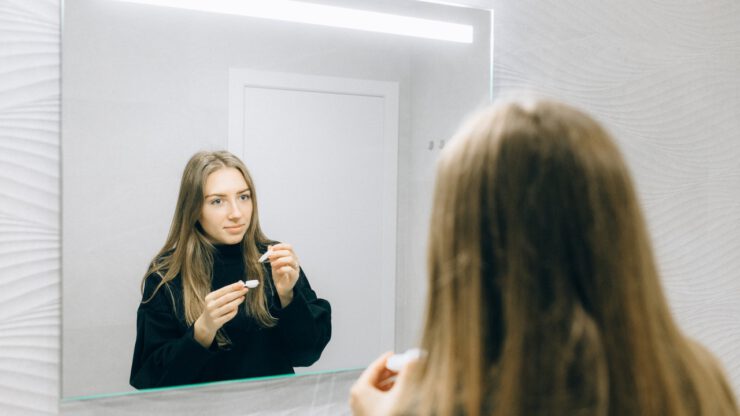 Kobieta przed lustrem w łazience zakłąda szkła kontaktowe