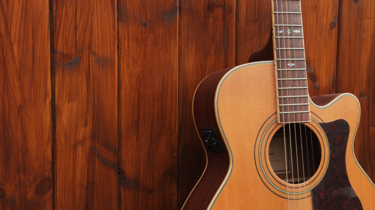 Gitara akustyczna oparta o drewnianą ścianę